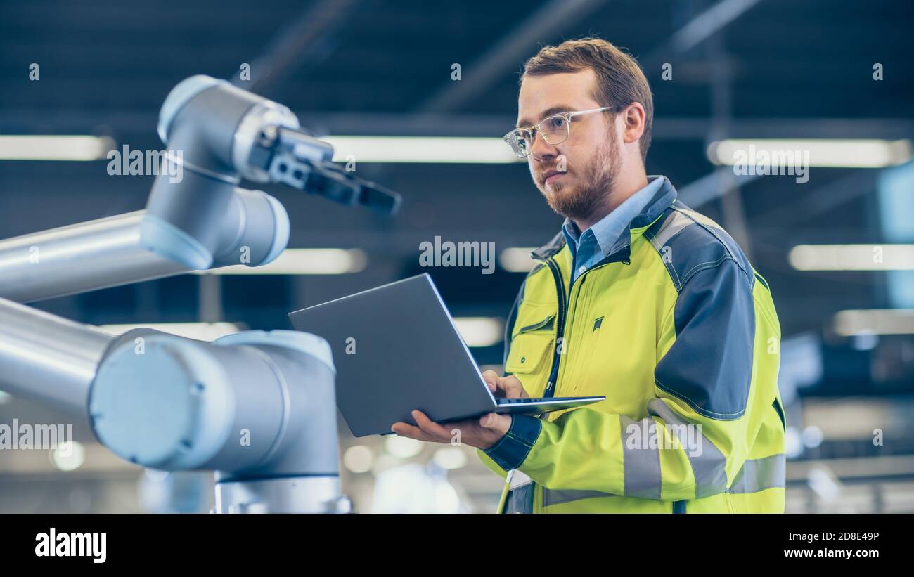 At the Factory: Automation Engineer Uses Laptop for Programming Robotic ...