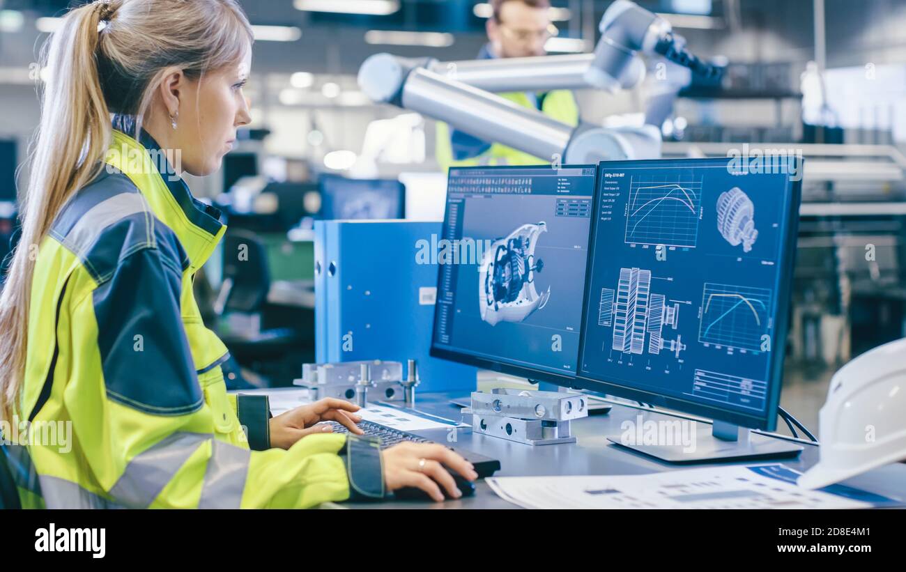At the Factory: Female Mechanical Engineer Designs 3D Engine on Her Personal Computer, Male Automation Engineer Uses Laptop for Programming Robotic Stock Photo
