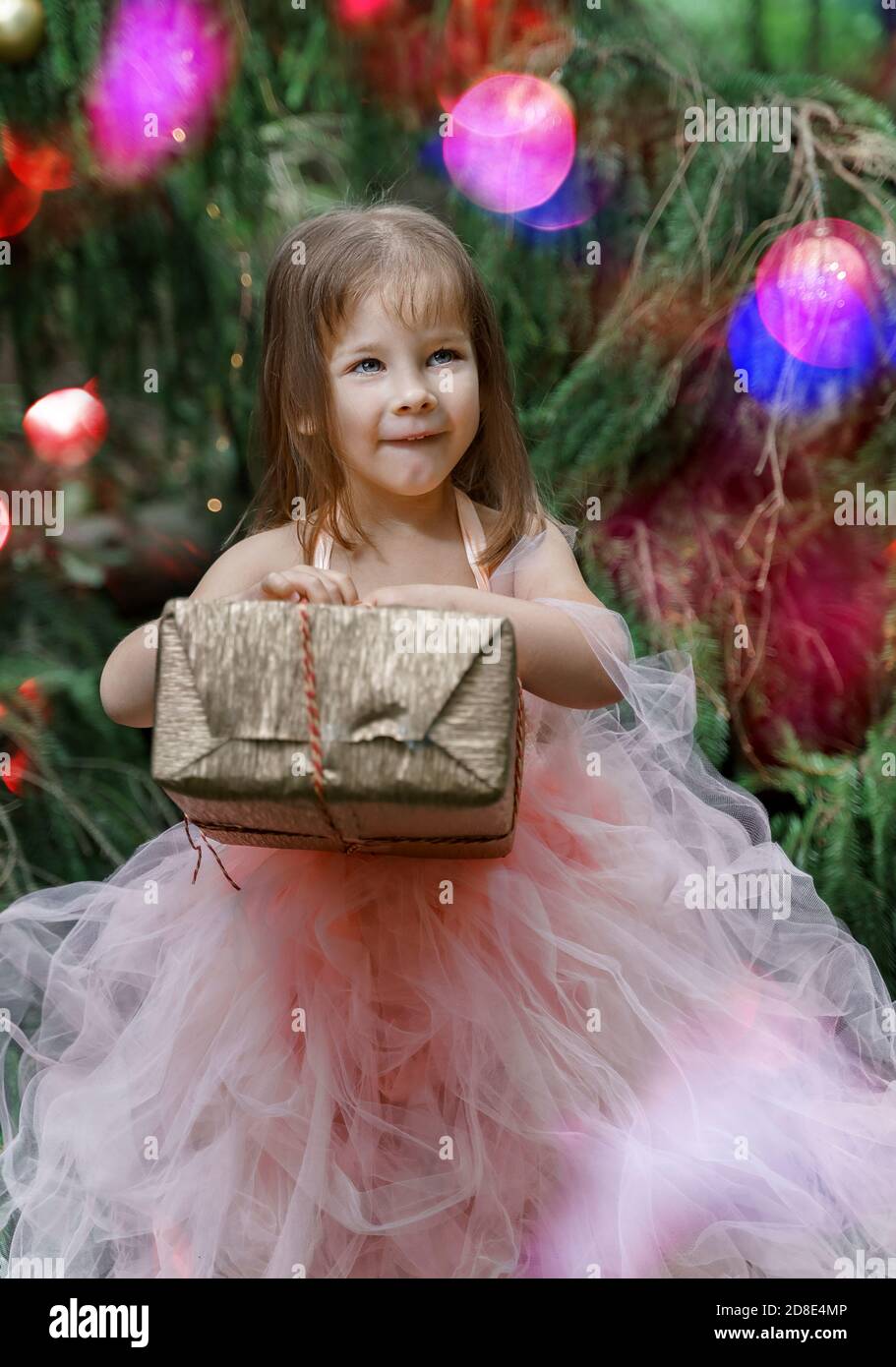 cute little girl in a pink dress with a gift box by the christmas tree ...