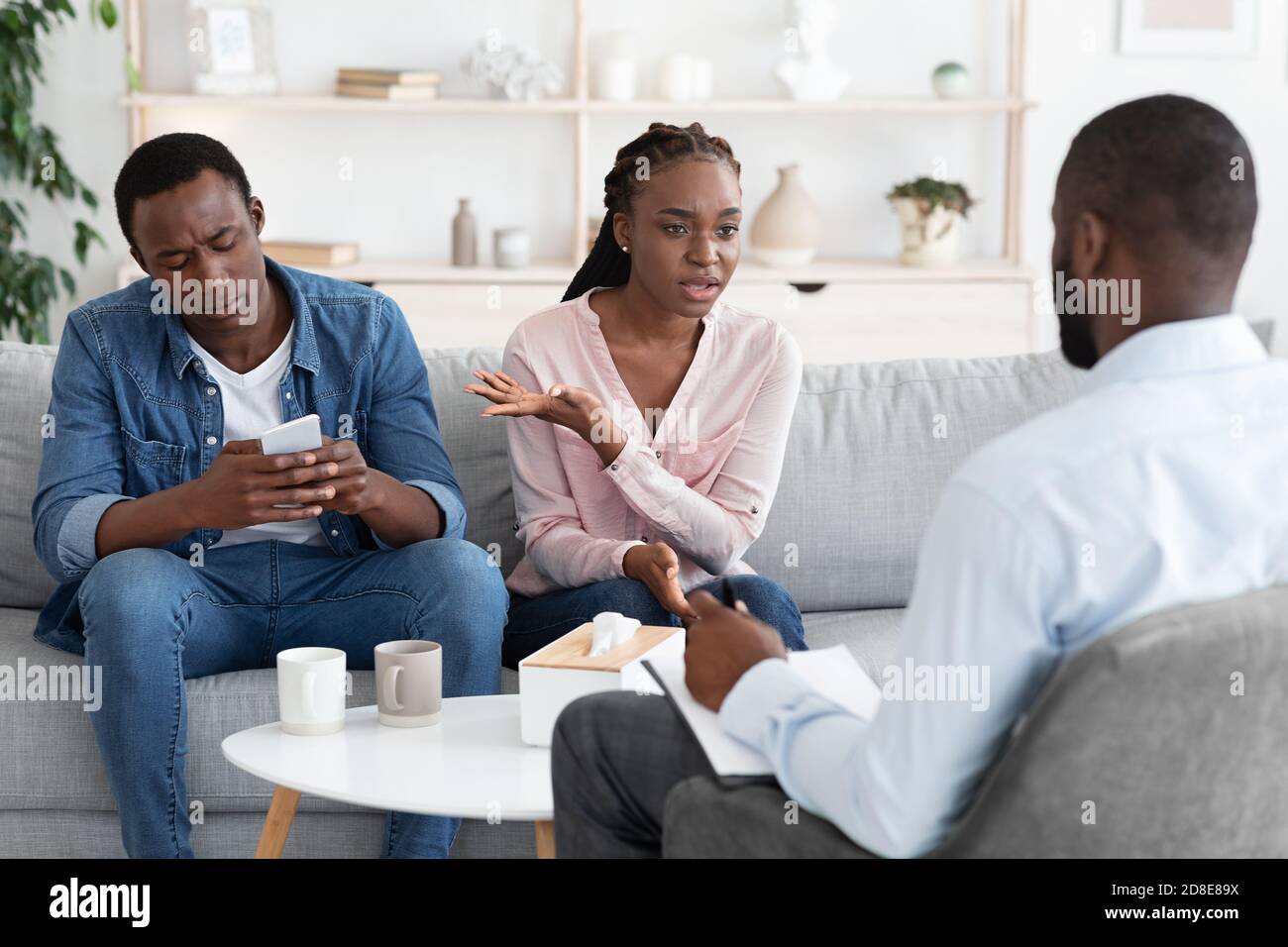 Smartphone Addiction. Annoyed African Wife Complaining About Indifferent Husband To Family Counselor Stock Photo