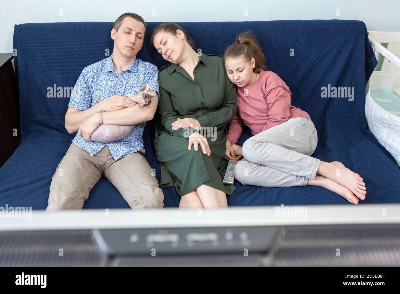 Caucasian bored family fell a sleep while watching movie at home on weekend, father, mother, teen age daughter and sphynx cat Stock Photo