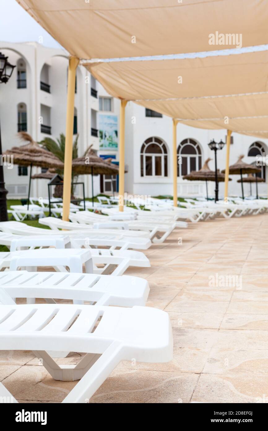 A lot of empty white plastic sunbeds are on terrace of a hotel area