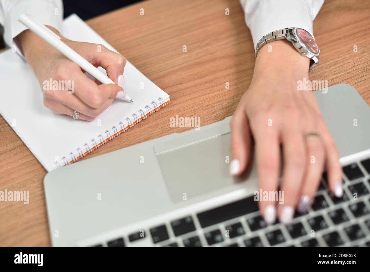 Closeup of female hands writing in notepad and typing on laptop