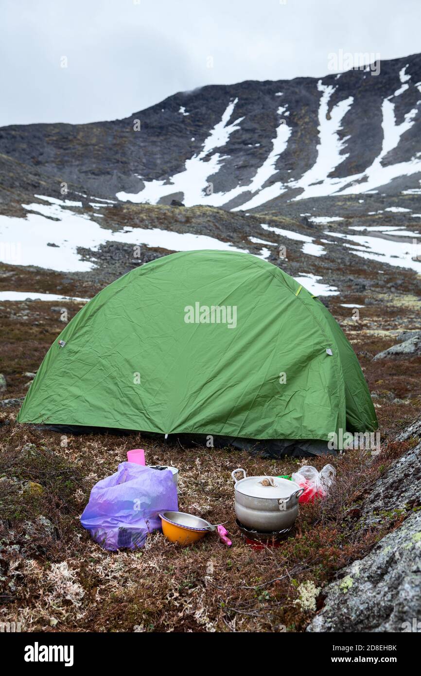 Food cooking on portable gas stove during hiking, green tent is on mountain  valley for sleeping, mountains with severe weather and snow patches Stock  Photo - Alamy