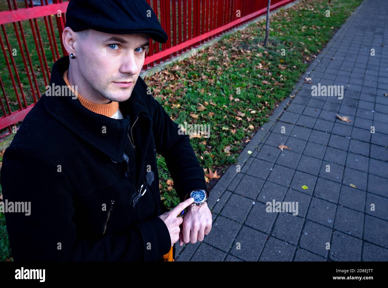 Portrait of a young man in black coat, pointing impatiently on his wristwatch, waiting for a date and looking angry at camera. You are late, hurry up! Stock Photo