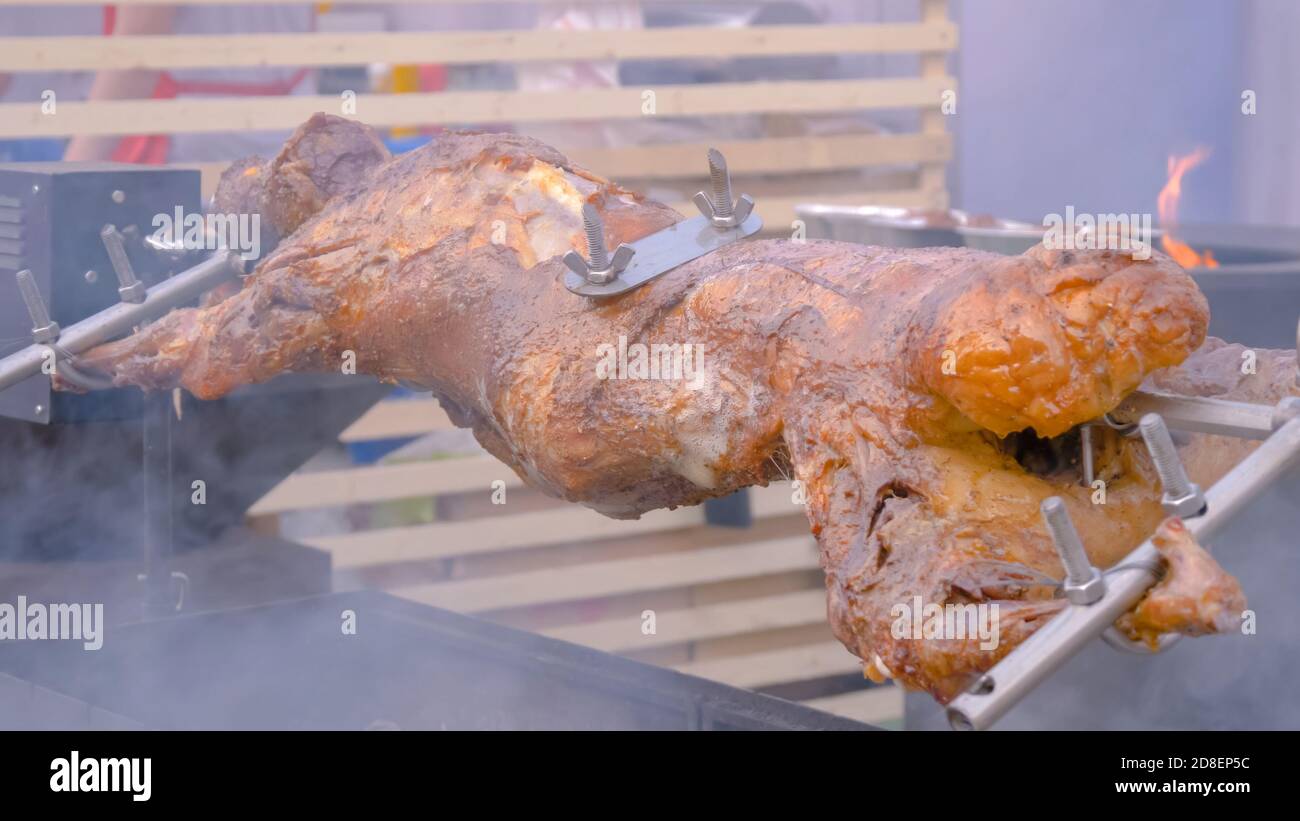 Process of cooking roasted pork on spit at summer outdoor food market - close up view. Professional cooking, catering, cookery, gastronomy and street Stock Photo