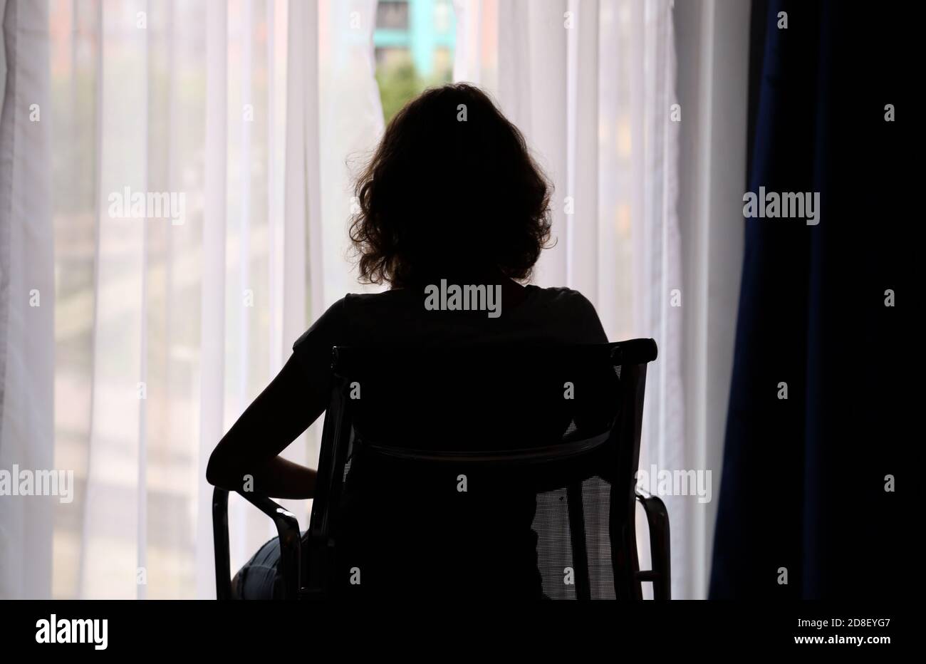 Rear view of silhouette girl sitting on a chair and looking through window at home Stock Photo
