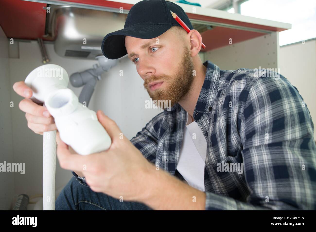 man repairs something inside kitchen cabinet under the sink Stock Photo