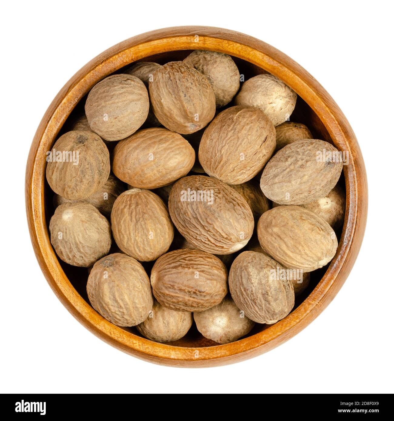 Dried whole nutmegs in a wooden bowl. Fragrant or true nutmeg, seed of Myristica fragrans with distinctive pungent fragrance, used as spice. Stock Photo