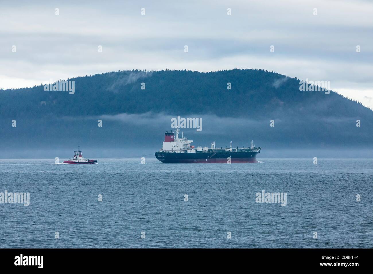 A oil freighter being escorted by a tugboat south of Cypress island in the San Juan Islands on a cloudy day, Rosario Strait, Washington, USA. Stock Photo