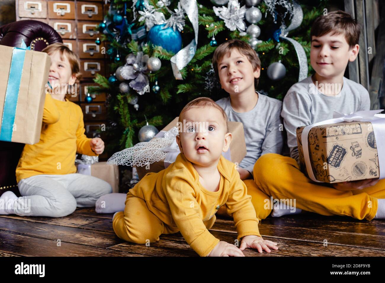 Happy children brothers opening gifts in front of Christmas tree. Christmas time. Focus on baby. Stock Photo