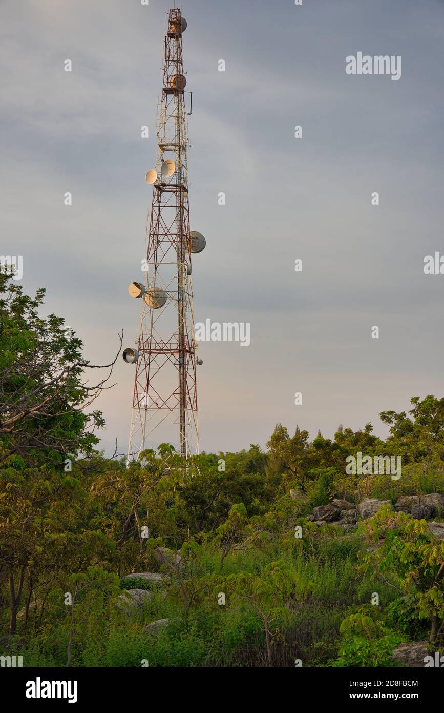 This unique photo shows a transmitter and telephone pole in Thailand standing on top of a mountain in the middle of nature at sunset Stock Photo