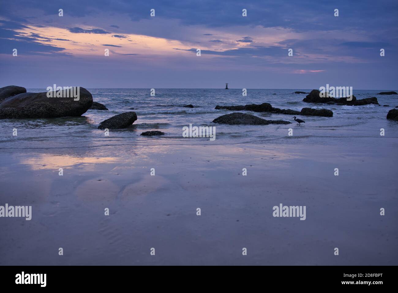 This unique photo shows the sunrise on Hua Hin Beach. You can see the first rays of the sun through the clouds and the big rocks on the beach Stock Photo