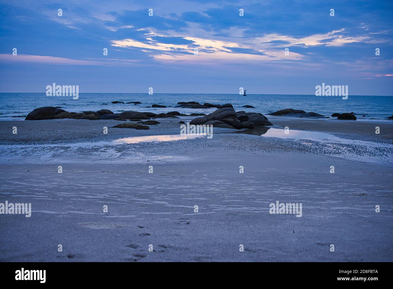 This unique photo shows the sunrise on Hua Hin Beach. You can see the first rays of the sun through the clouds and the big rocks on the beach Stock Photo