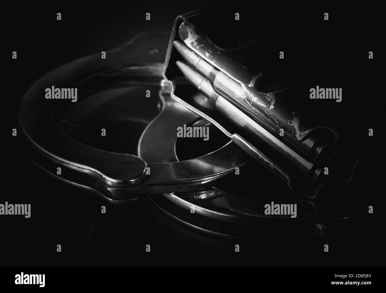 A rifle magazine loaded with 223 caliber bullets on top of a set of handcuffs on a black background Stock Photo
