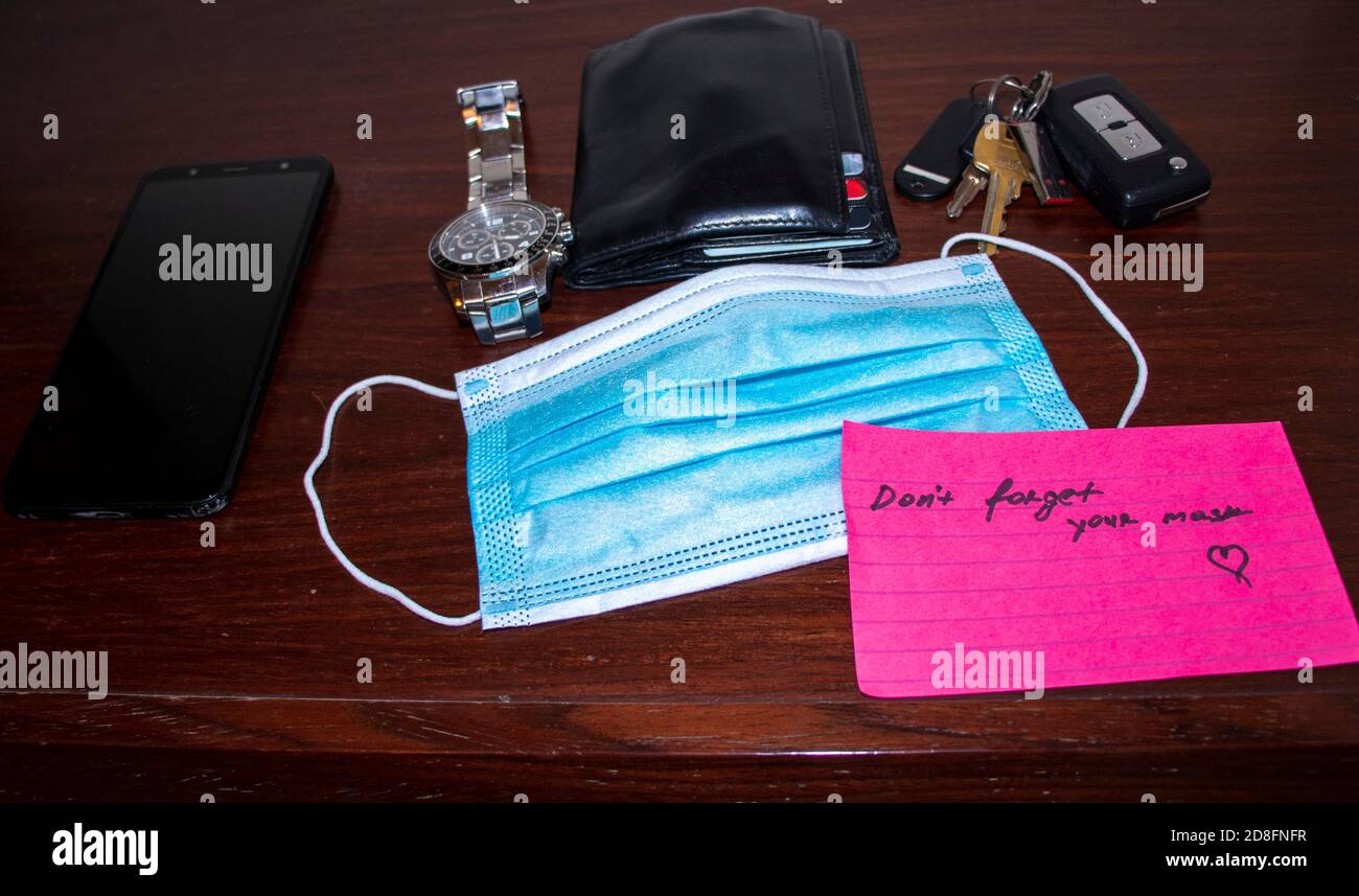 New reality. Picture of a phone, keys, wallet, watch surgical mask and note on side table Stock Photo
