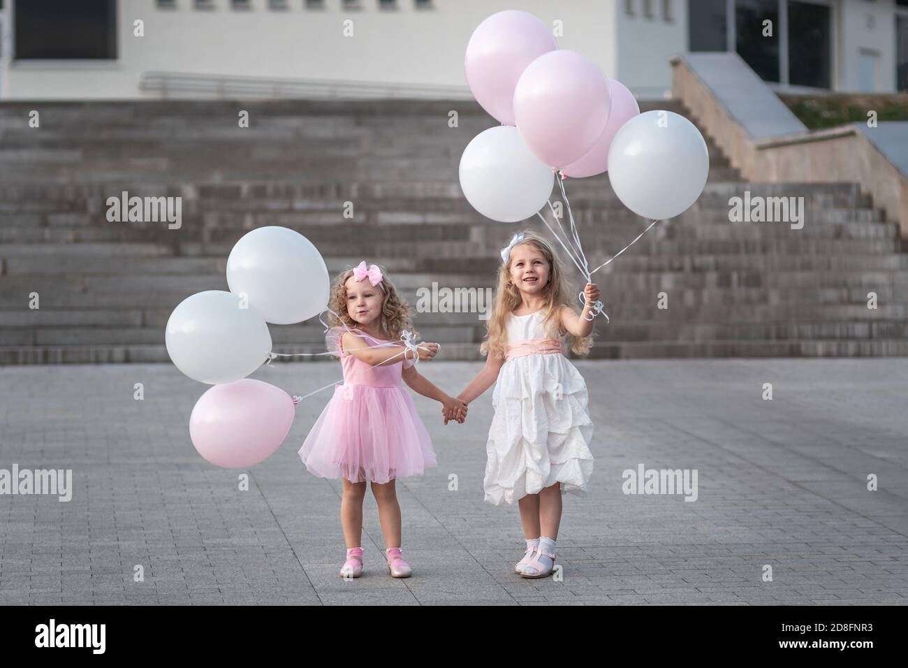Two little girls in pink and white dressses with balloons walking on ...