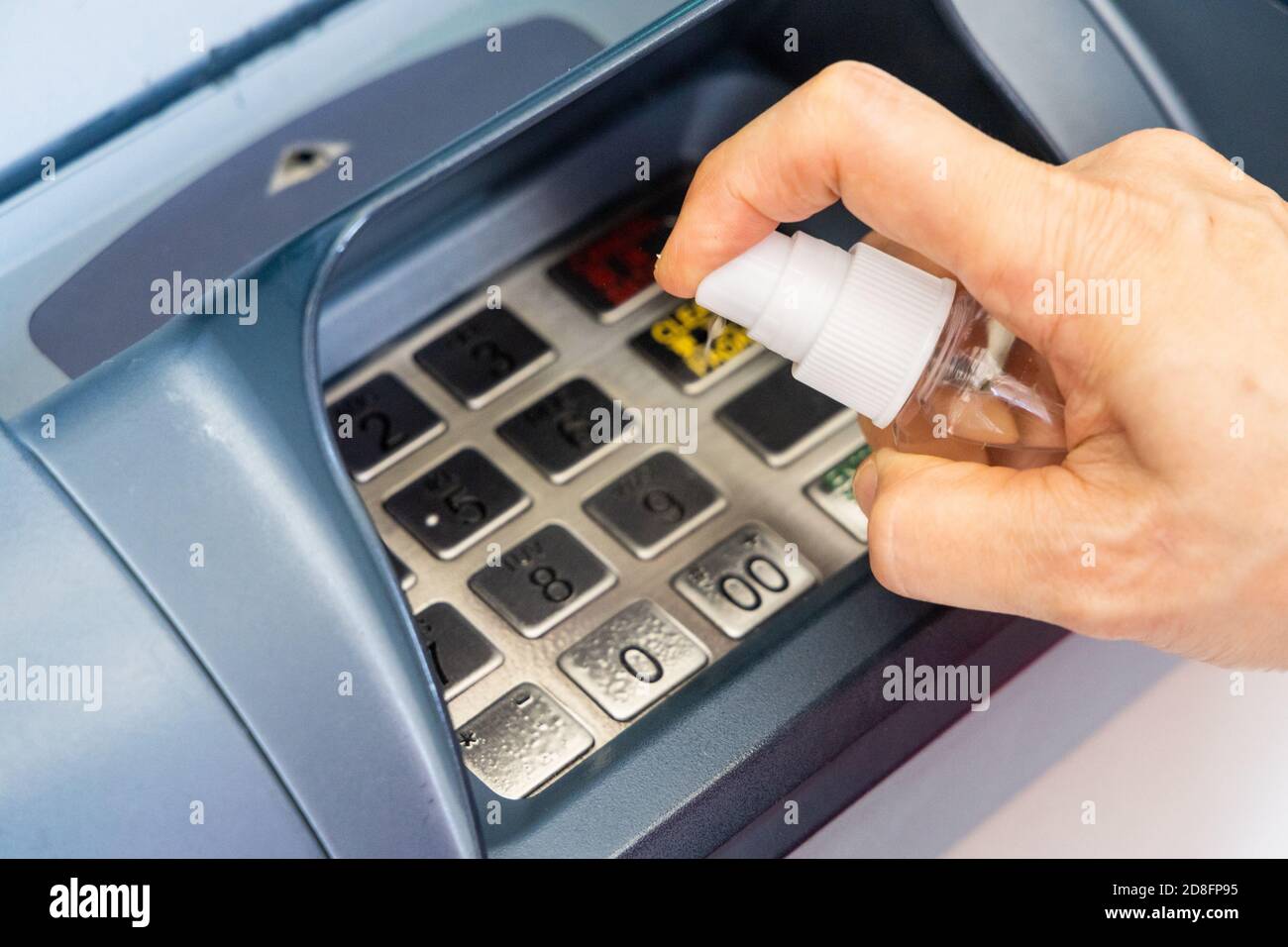 Person spraying sanitizer disinfectant onto ATM key pad to kill germs Stock Photo