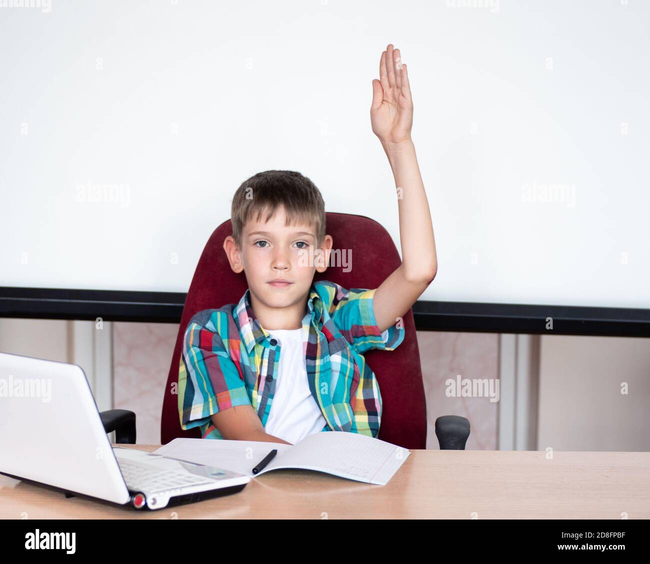 A smart, cute boy raises his hand to answer in class. Happy child against a white board, concept back to school Stock Photo