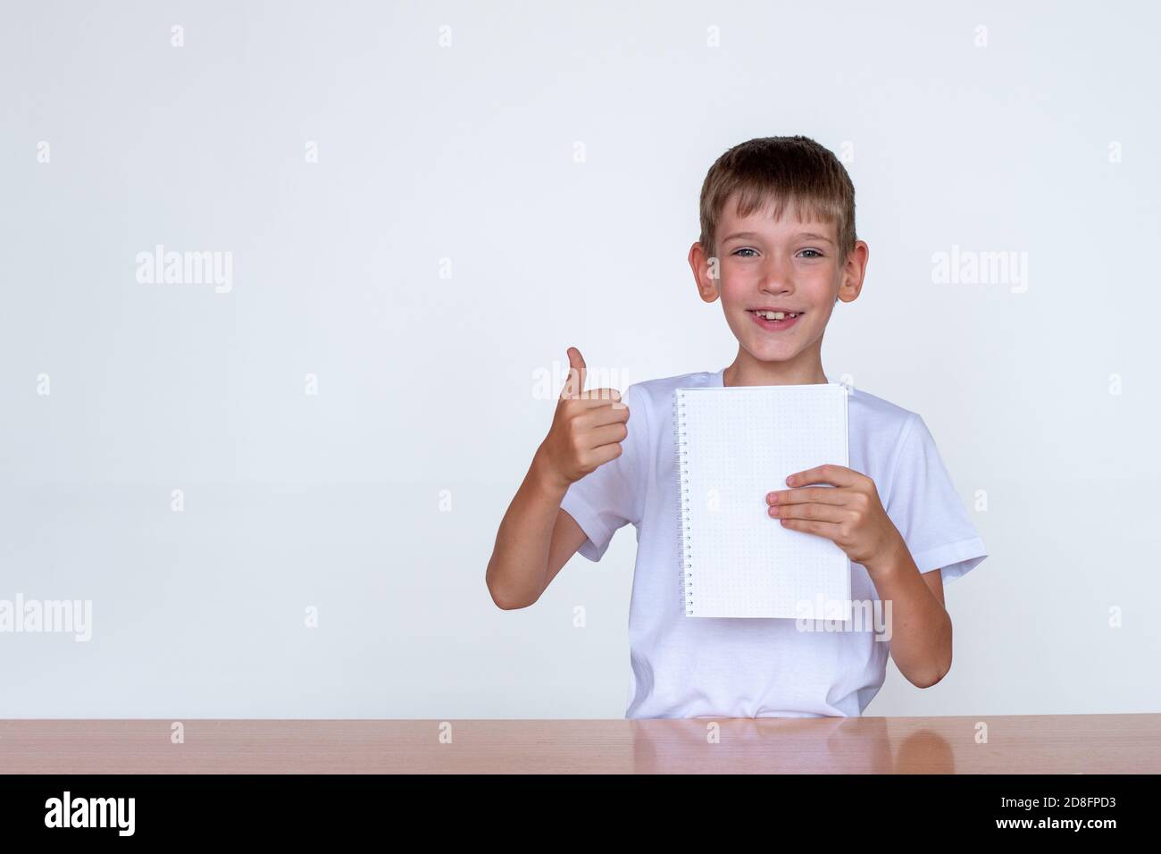 Portrait of a cute caucasian boy holding a white notebook in his hand, showing thumbs up. Concept for back to school Stock Photo