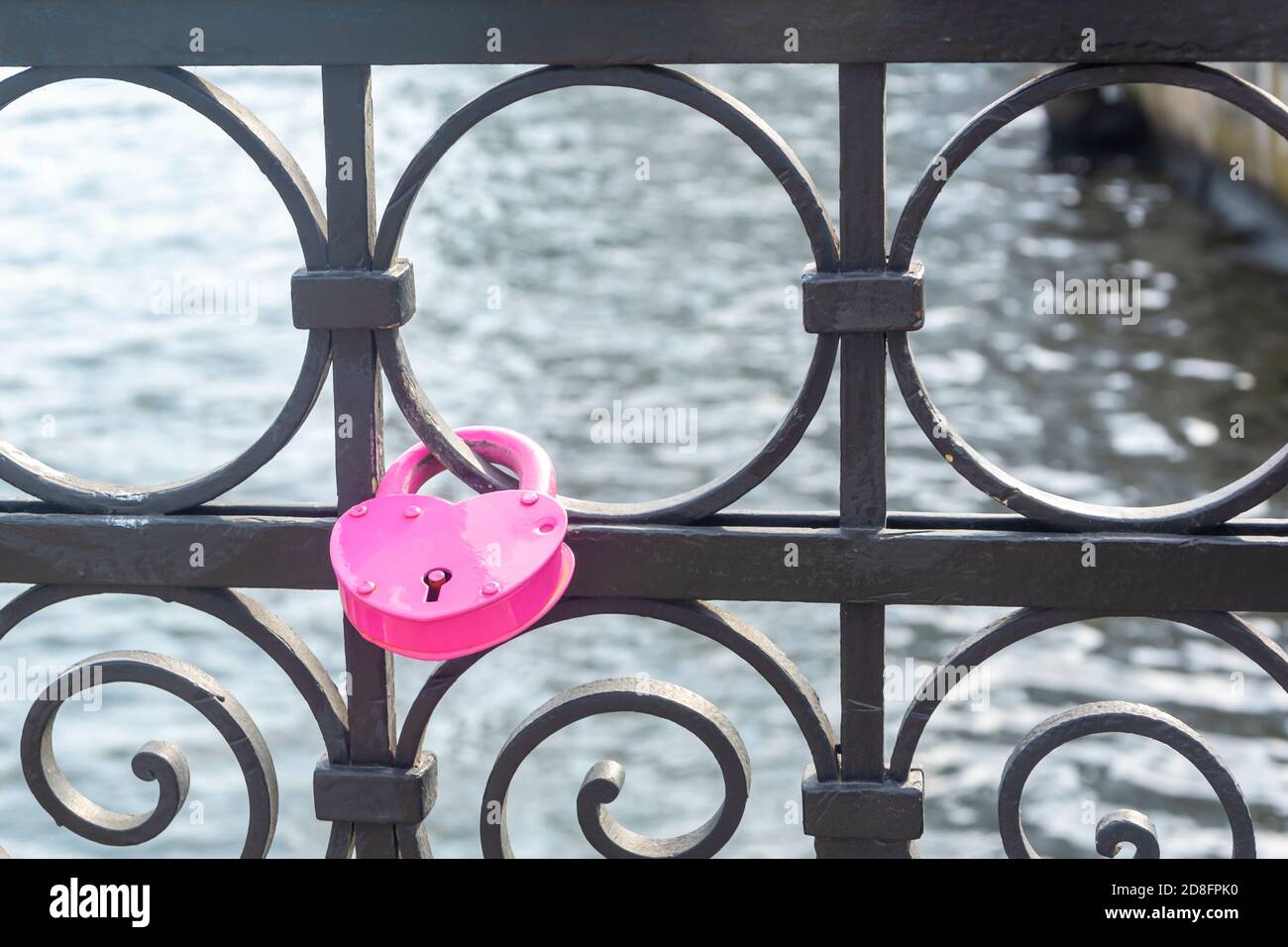 Pink padlock in the shape of heart closed by newlyweds on their wedding day. Symbol of eternal love and fidelity on forged metal fence of bridge. Stock Photo
