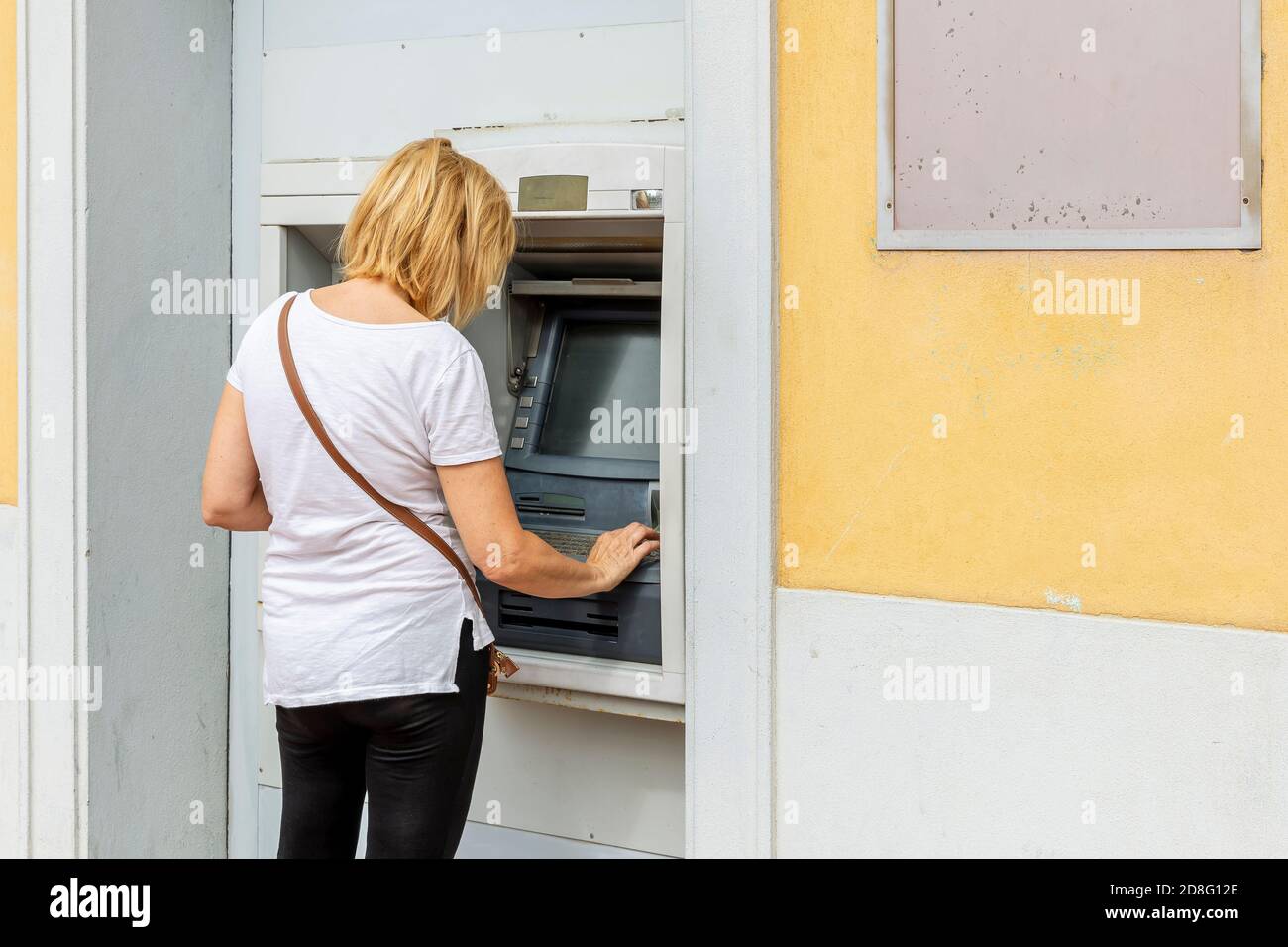 Blond white woman withdraws cash from an ATM Stock Photo