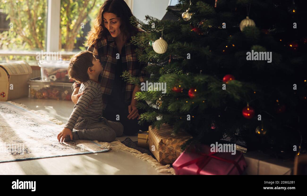 Mother with her child celebrating Christmas. Woman with her son sitting beside decorated Christmas tree with lots of gift boxes.; Stock Photo