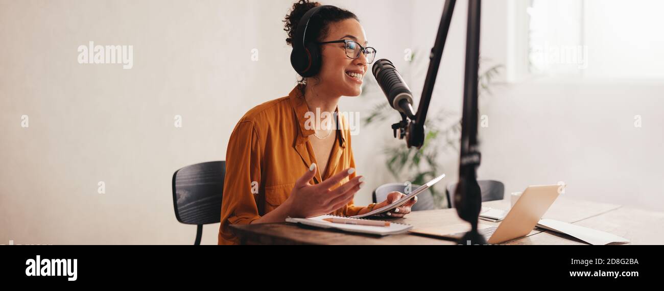 Woman recording a podcast on her laptop computer with headphones and a microscope. Female podcaster making audio podcast from her home studio. Stock Photo