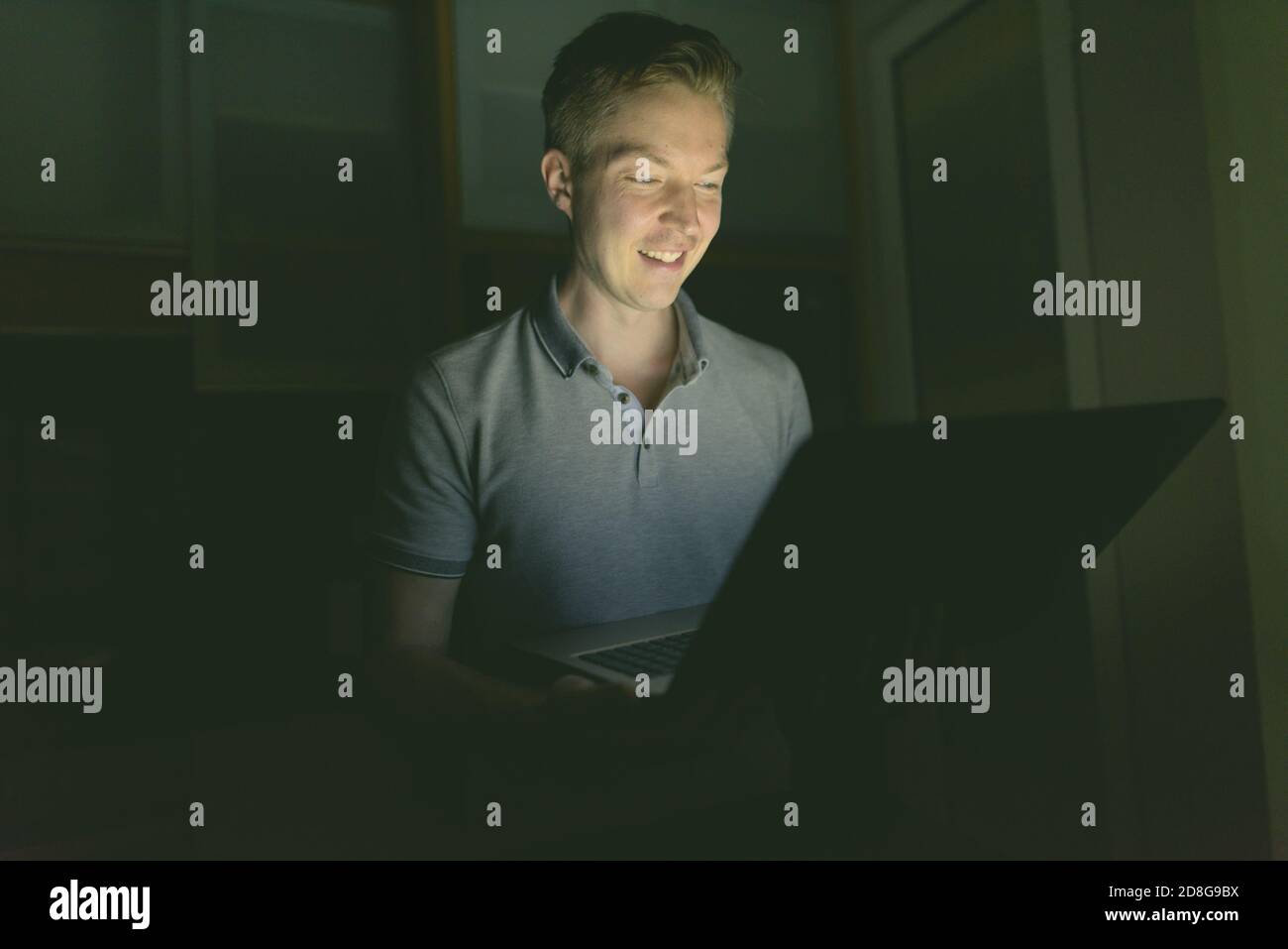 Young handsome man using laptop in the dark living room Stock Photo