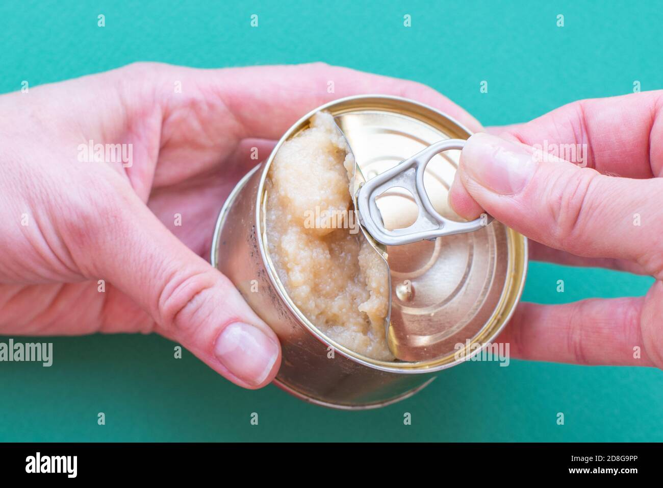 The hand of an adult man holds a can of canned food, the second hand opens the lid jerking a key Stock Photo