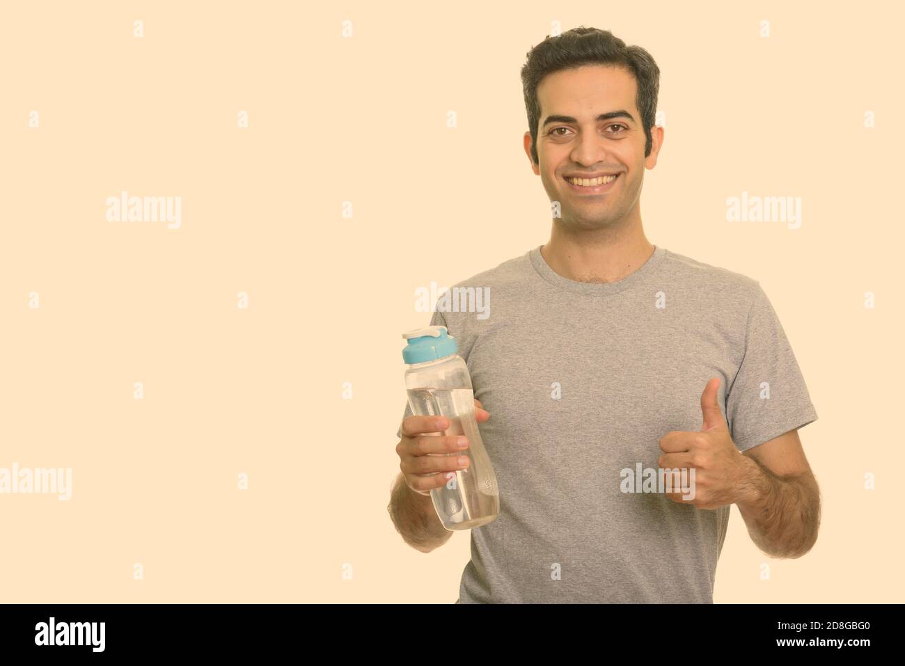 Young happy Persian man holding water bottle and giving thumb up ready ...