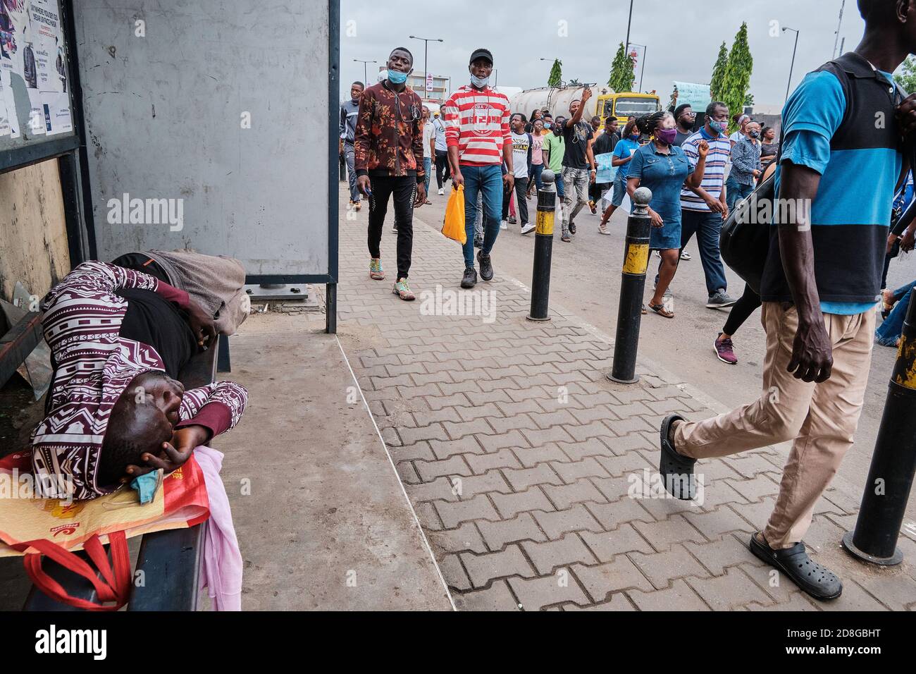 A man sleeps at a bus stop as protesters walk by during protests against police brutality tagged #EndSARS in Lagos Nigeria on October 17, 2020. Stock Photo