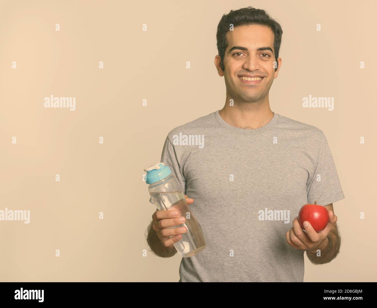 Young happy Persian man holding water bottle and red apple ready for ...