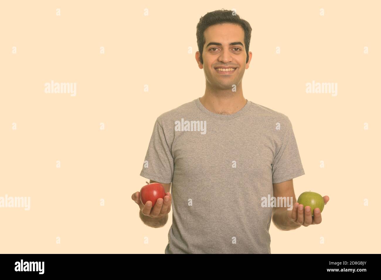Young happy Persian man holding red and green apple ready for gym Stock ...