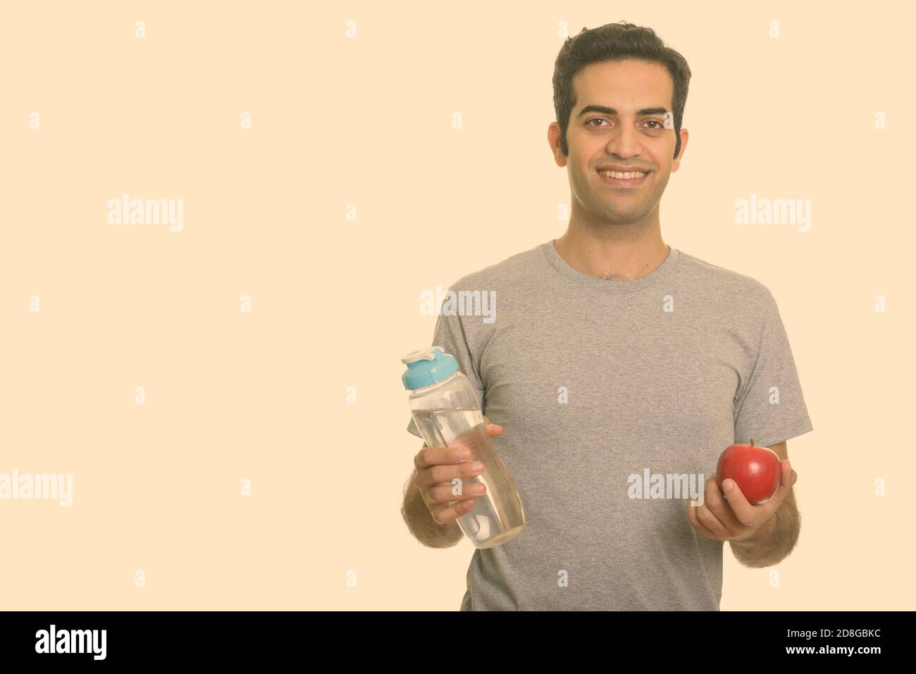 Young happy Persian man holding water bottle and red apple ready for ...