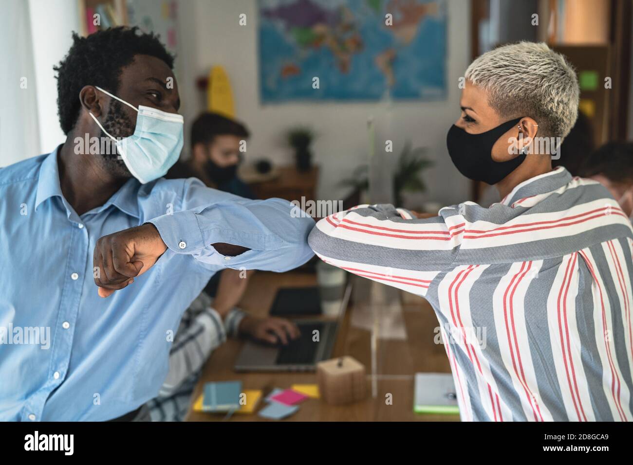 Young multiracial workers wearing face mask doing new social distance greetings bumping elbows inside co-working creative space Stock Photo