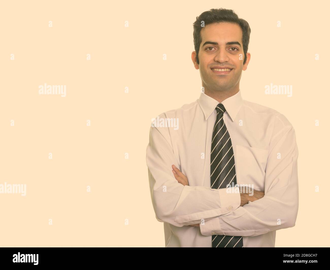 Portrait of happy young Persian businessman smiling with arms crossed ...