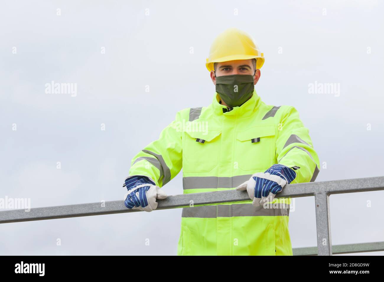 Portrait of smiling young engineer or worker with face mask and hard hat and protective work wear Stock Photo