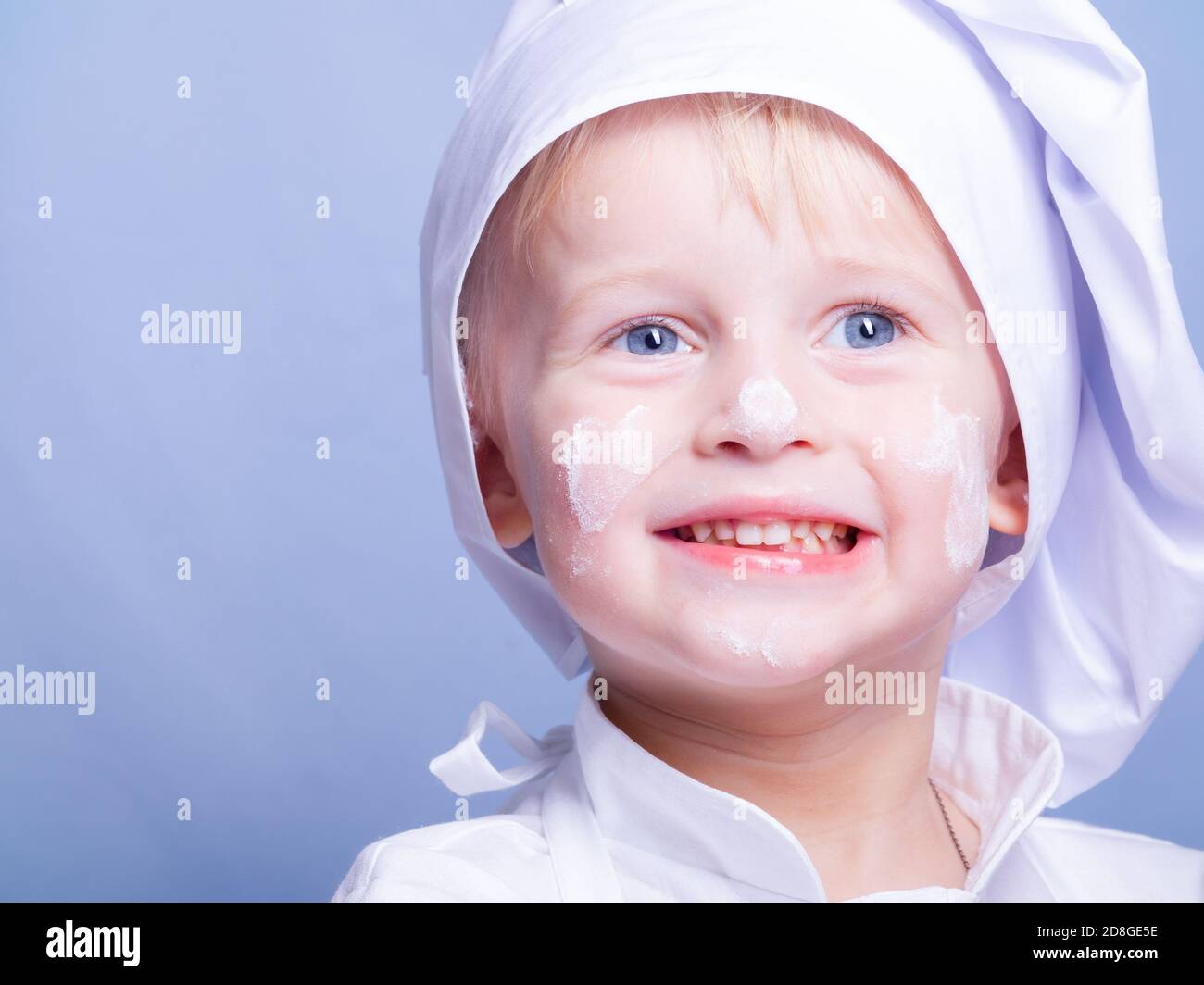 a 3yearold boy in a suit and a chef's cap smiles at the camera Stock