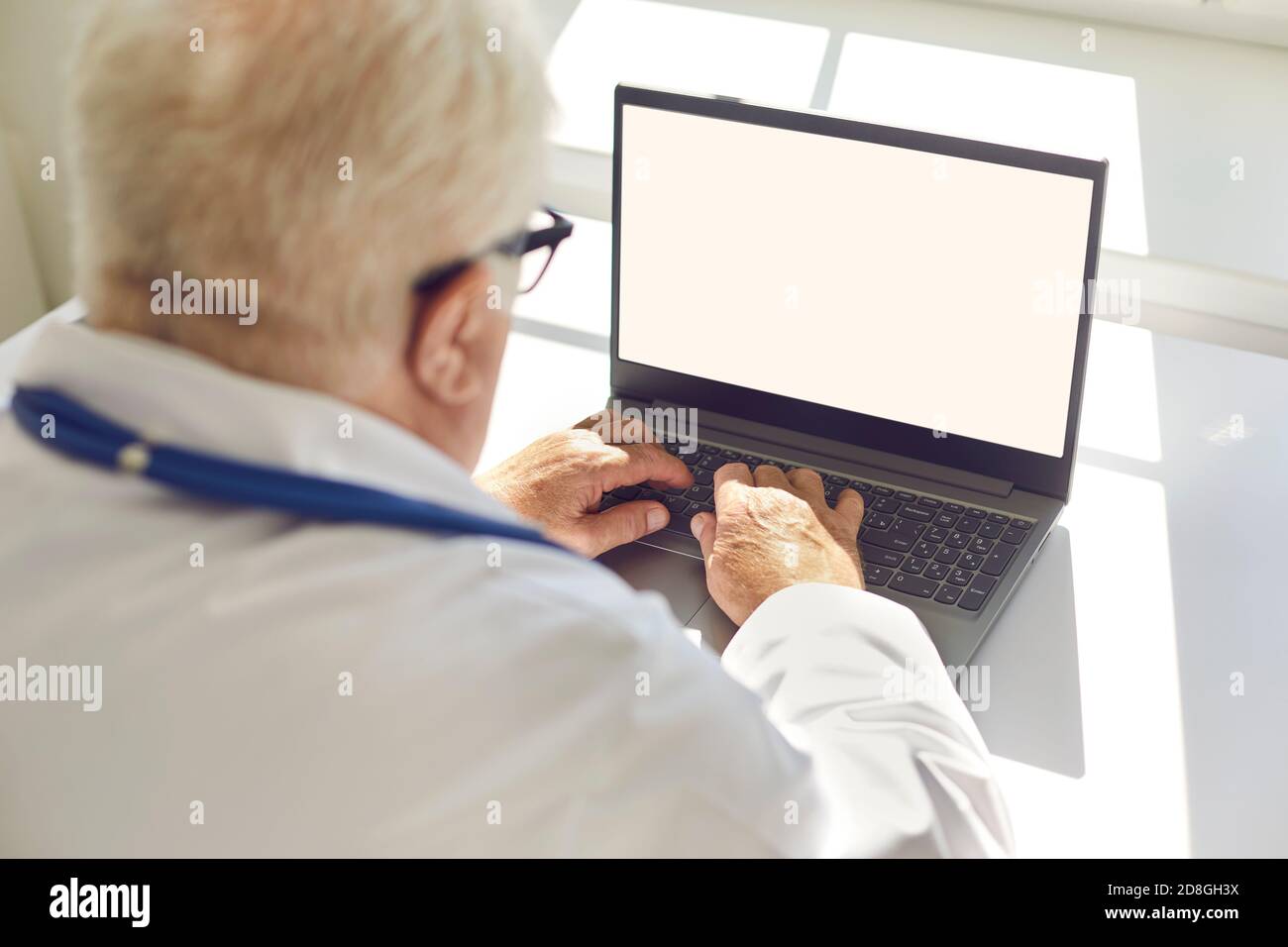 Senior man sitting in a bright room behind a laptop and typing on the keyboard. Close up. Stock Photo