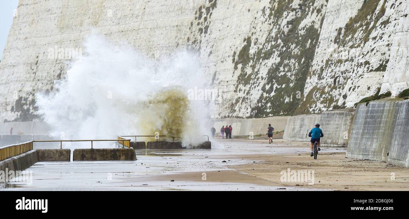 Brighton UK 30th October 2020 - A cyclist passes by waves crashing over the undercliff walk at Saltdean near Brighton this morning . Warnings have been issued that stormy weather is forecast for many parts of the UK this coming weekend : Credit Simon Dack / Alamy Live News Stock Photo