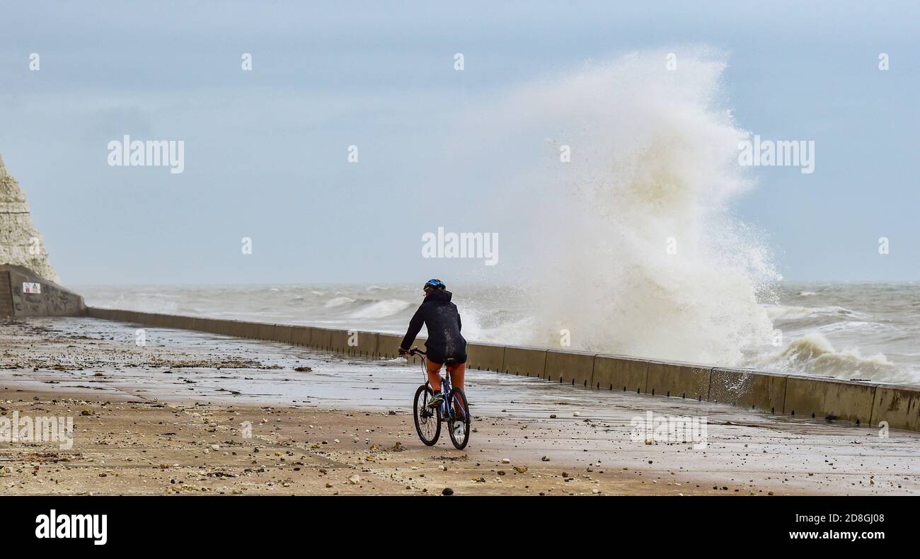 Brighton UK 30th October 2020 - A cyclist passes by waves crashing over the undercliff walk at Saltdean near Brighton this morning . Warnings have been issued that stormy weather is forecast for many parts of the UK this coming weekend : Credit Simon Dack / Alamy Live News Stock Photo