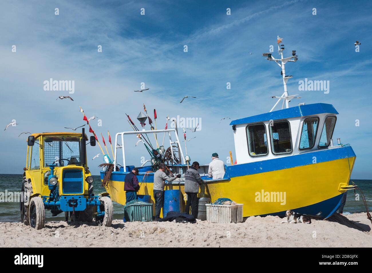 Workers arranging the network next to a fishing boat on the beach. Stock Photo