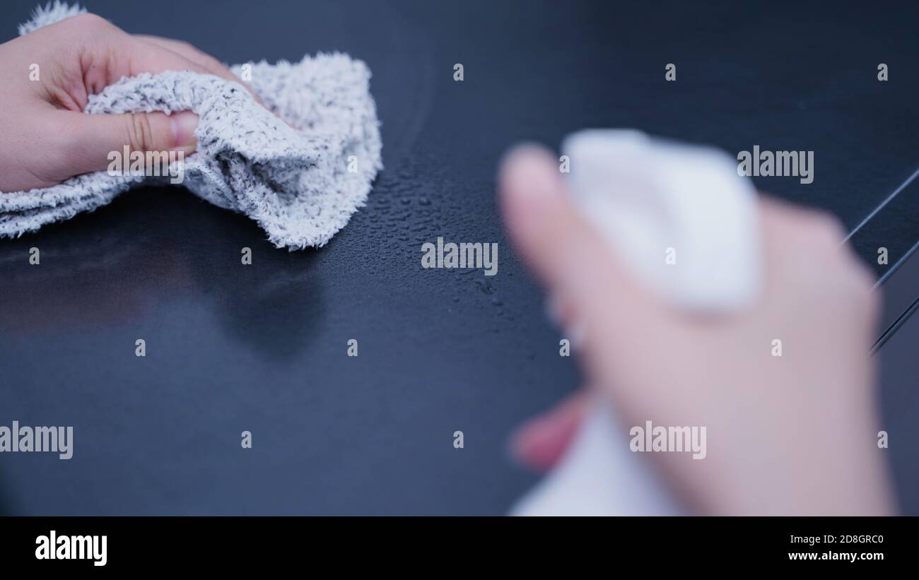 Young woman housekeeper in apron is cleaning, wiping down table surface ...