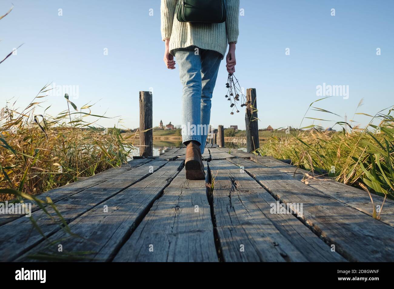 Unrecognizable woman traveler walking on old wooden bridge with bouquet dried flowers Stock Photo