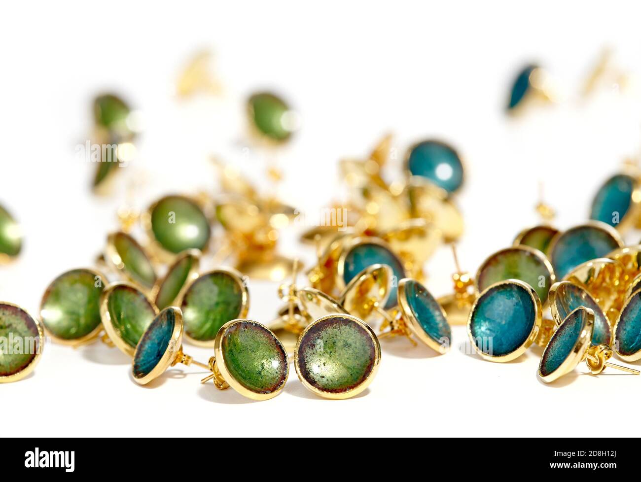 Handmade enamel jewelry by Kiln Design Studio. Seen here are several scattered gold stud earrings with blue or green enamel photographed on a white ba Stock Photo