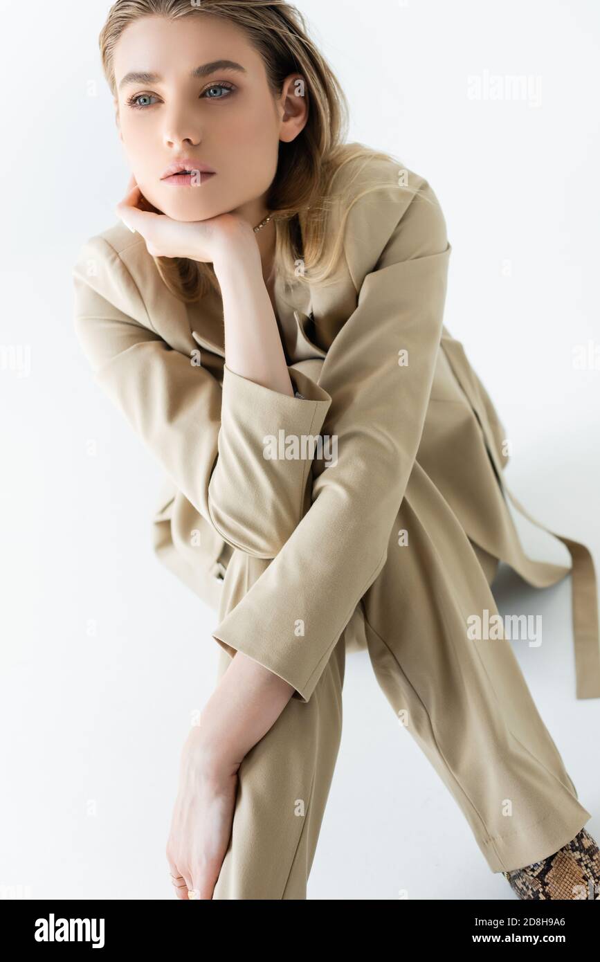 stylish and dreamy model in beige suit sitting on white Stock Photo