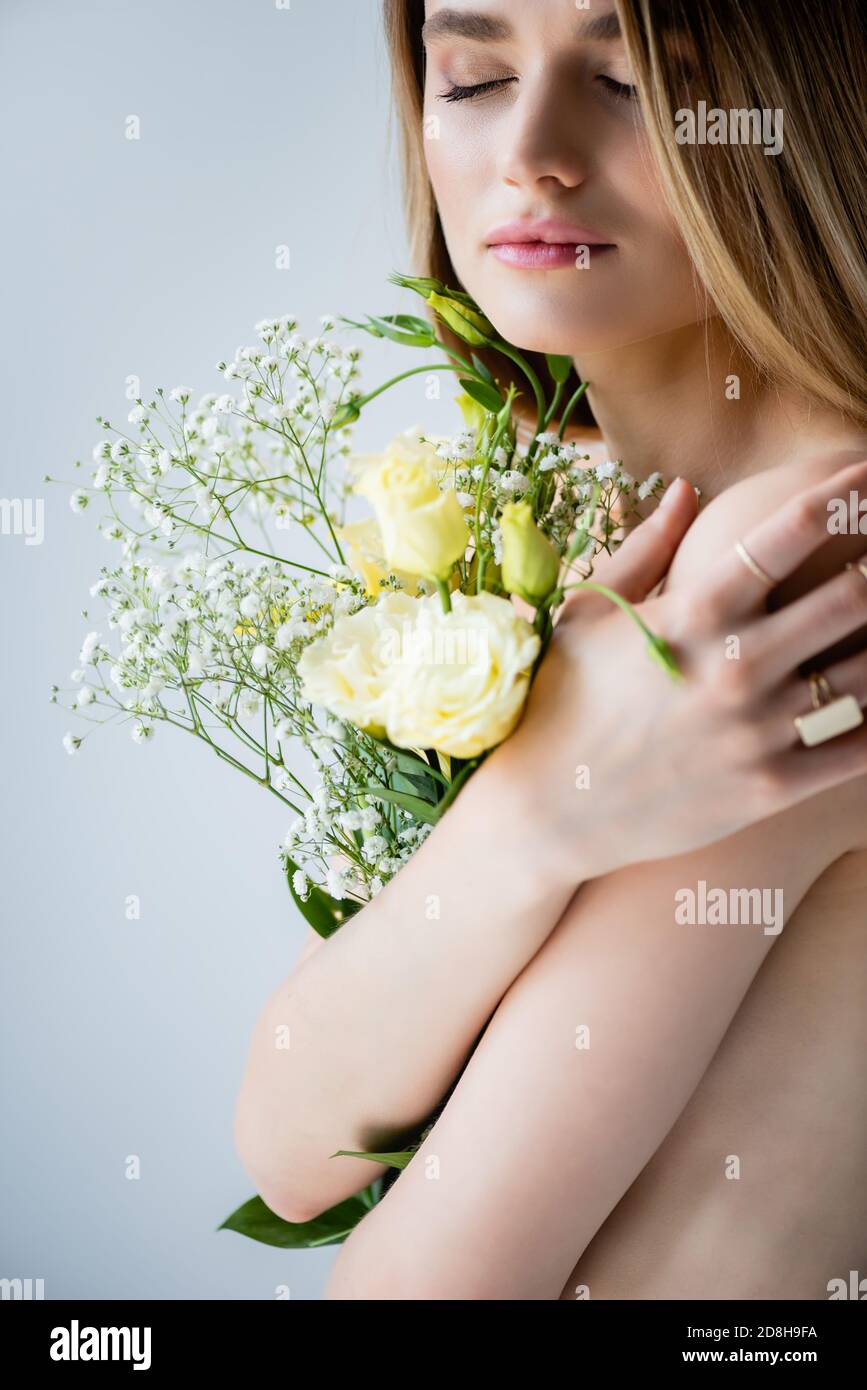 young model with closed eyes embracing flowers on grey Stock Photo