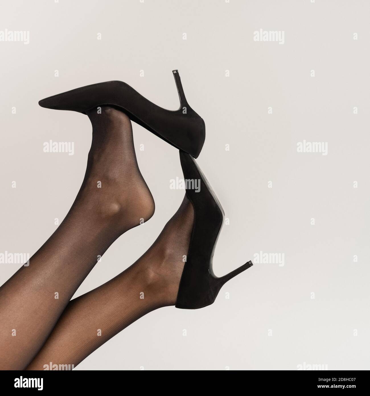 Cropped view of woman with legs in air, wearing black tights and shoes with heels isolated on grey Stock Photo
