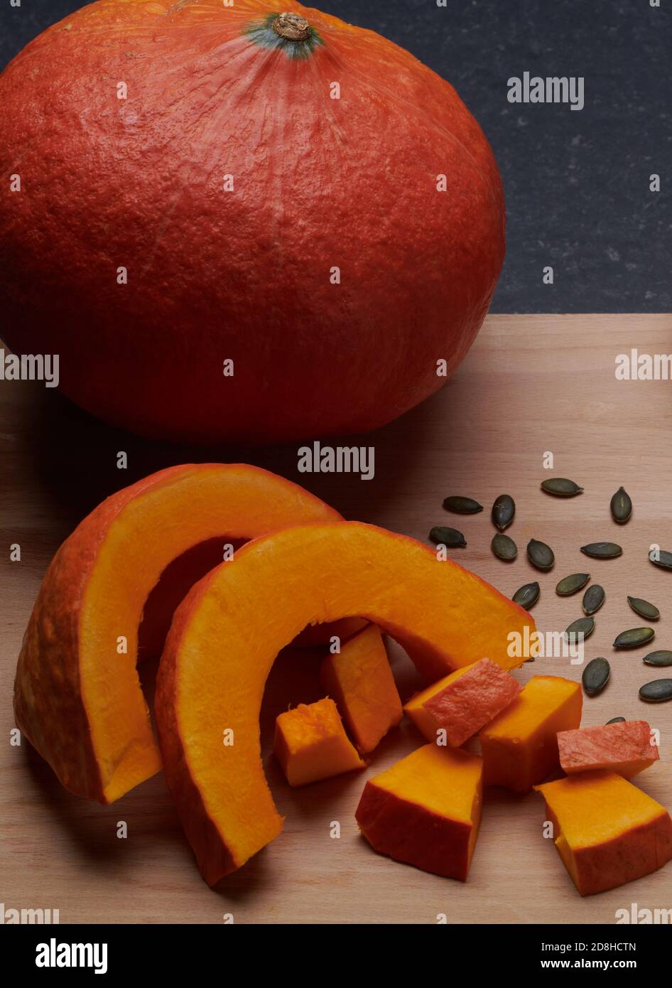 Orange round pumpkin, whole and sliced, with its seeds on a wooden cutting board Stock Photo